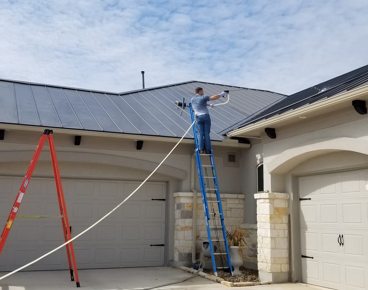 Applying soft wash to a metal roof from a ladder